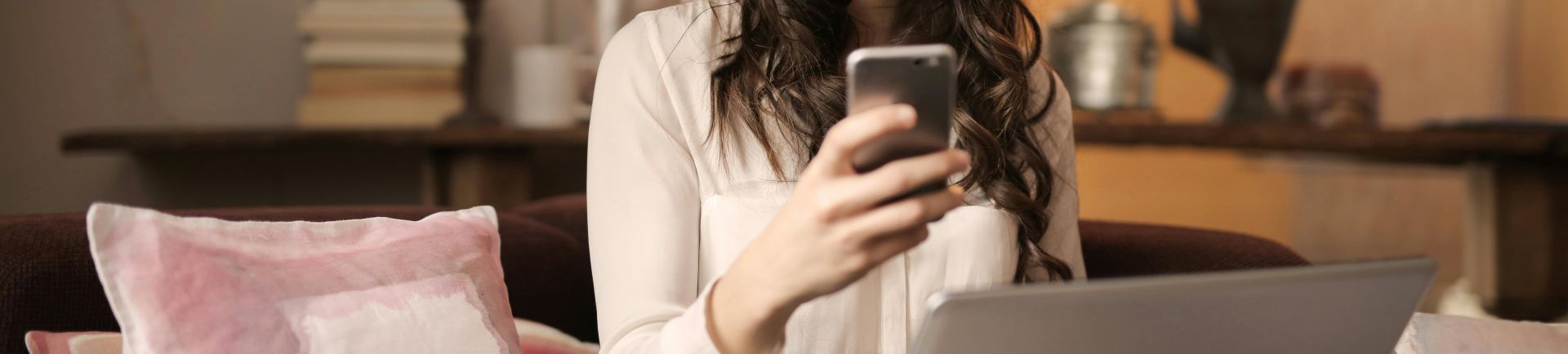 Woman Sitting on Sofa While Looking at Phone With Laptop on Lap